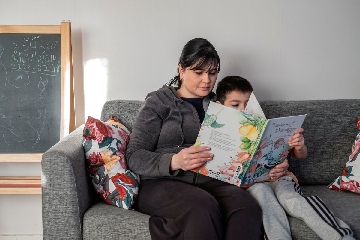 En kvinna och ett barn sitter i en soffa och läser en barnbok.
