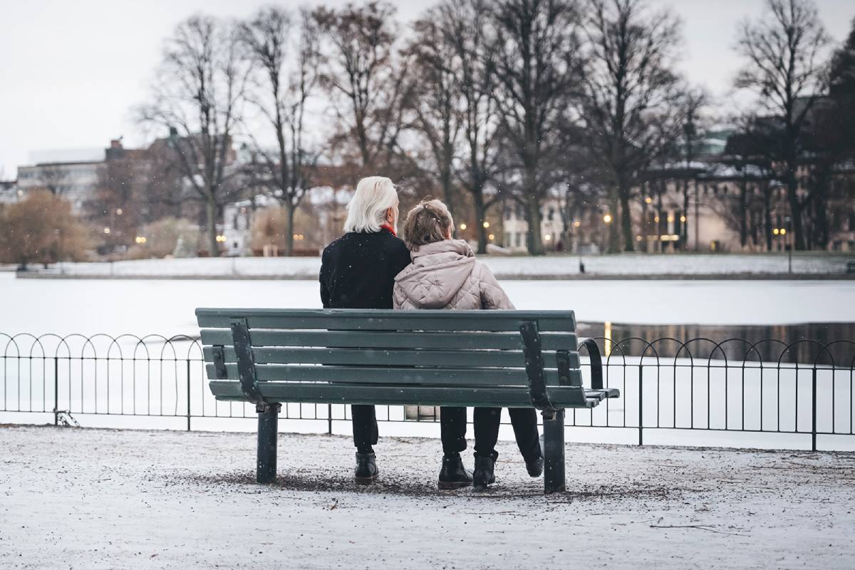 Ett äldre par sitter på en parkbänk och tittar ut över ett vinterlandskap.