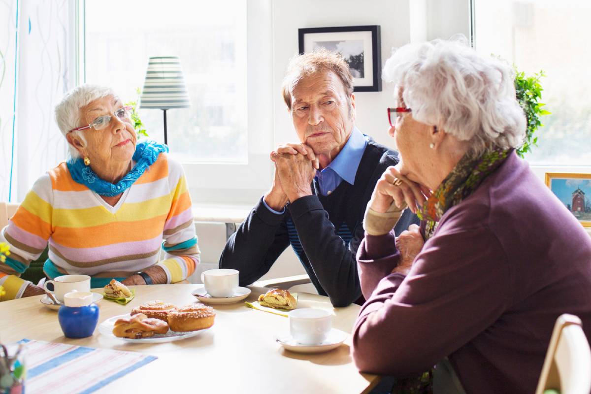 Tre äldre personer sitter vid ett bord och samtalar.